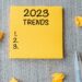 2023 Trends word on yellow note with pen and crumbled paper on wooden table background.